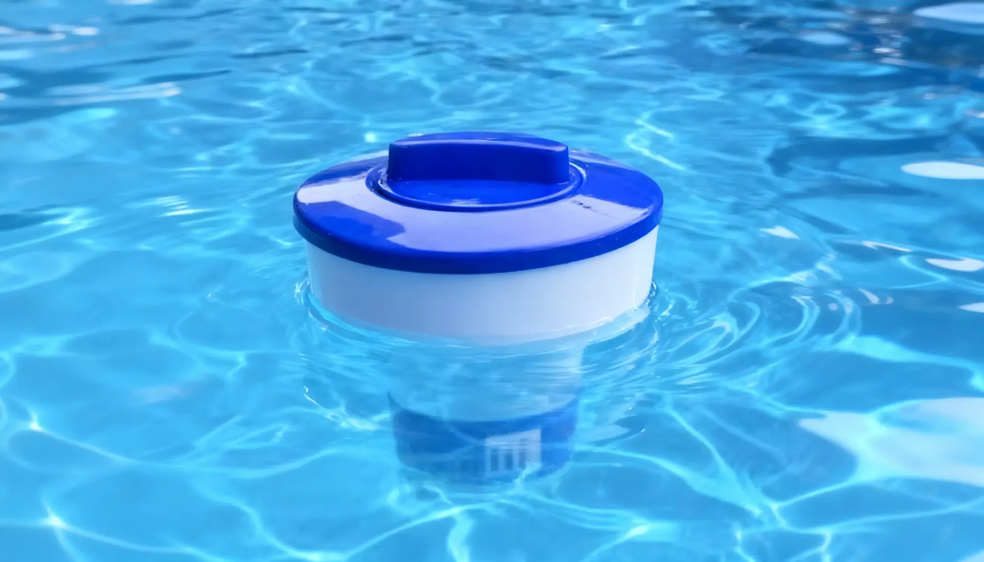 A white and blue floating chlorine tablet dispenser bobbing gently in the water, the recommended easy method for adding a slow, steady dose of chlorine to the pool.