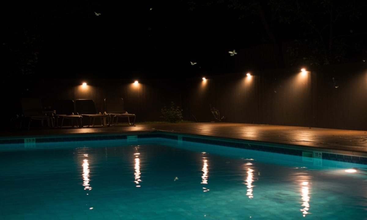 Bright white poolside lights attracting flying insects at night.