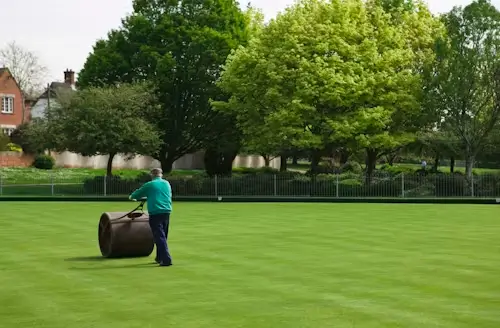 A person using a water-filled lawn roller to press newly laid sod firmly into the soil, eliminating air pockets for better root contact.