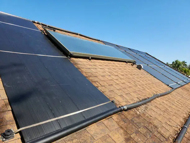 Close-up of solar pool heating collector panels installed on a shingled roof with connected pipes under bright sunlight.