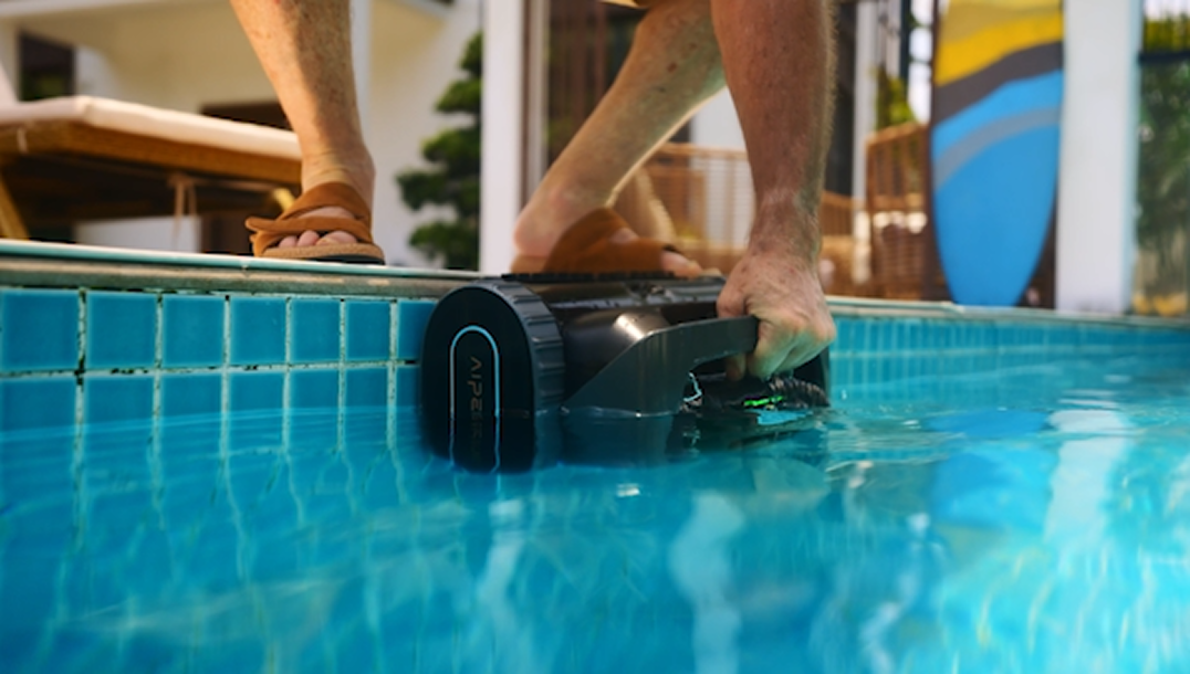 Man lifting Aiper robotic pool cleaner out of swimming pool before shock chlorination to avoid high chlorine damage.