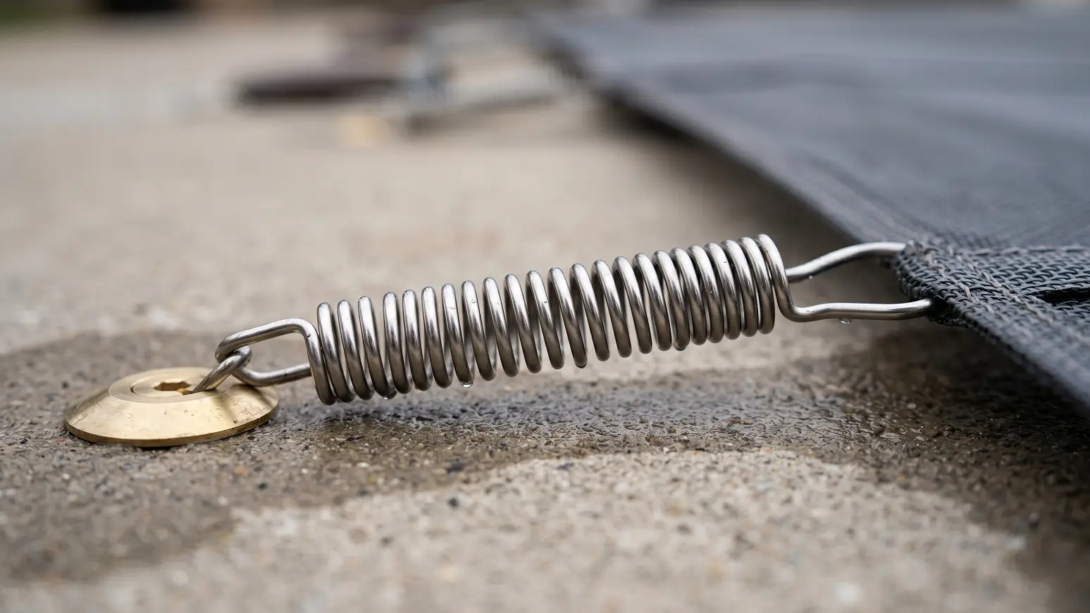 Close-up of a tightened stainless steel spring on an in-ground pool safety cover strap.