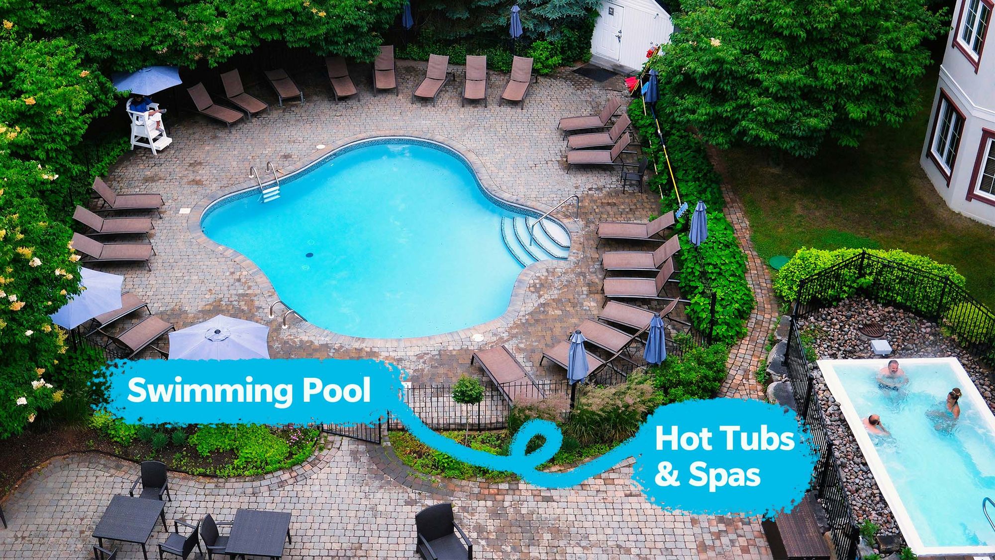 An aerial view of a hotel pool with hot tubs & spas, surrounded by lounge chairs and lush greenery.
