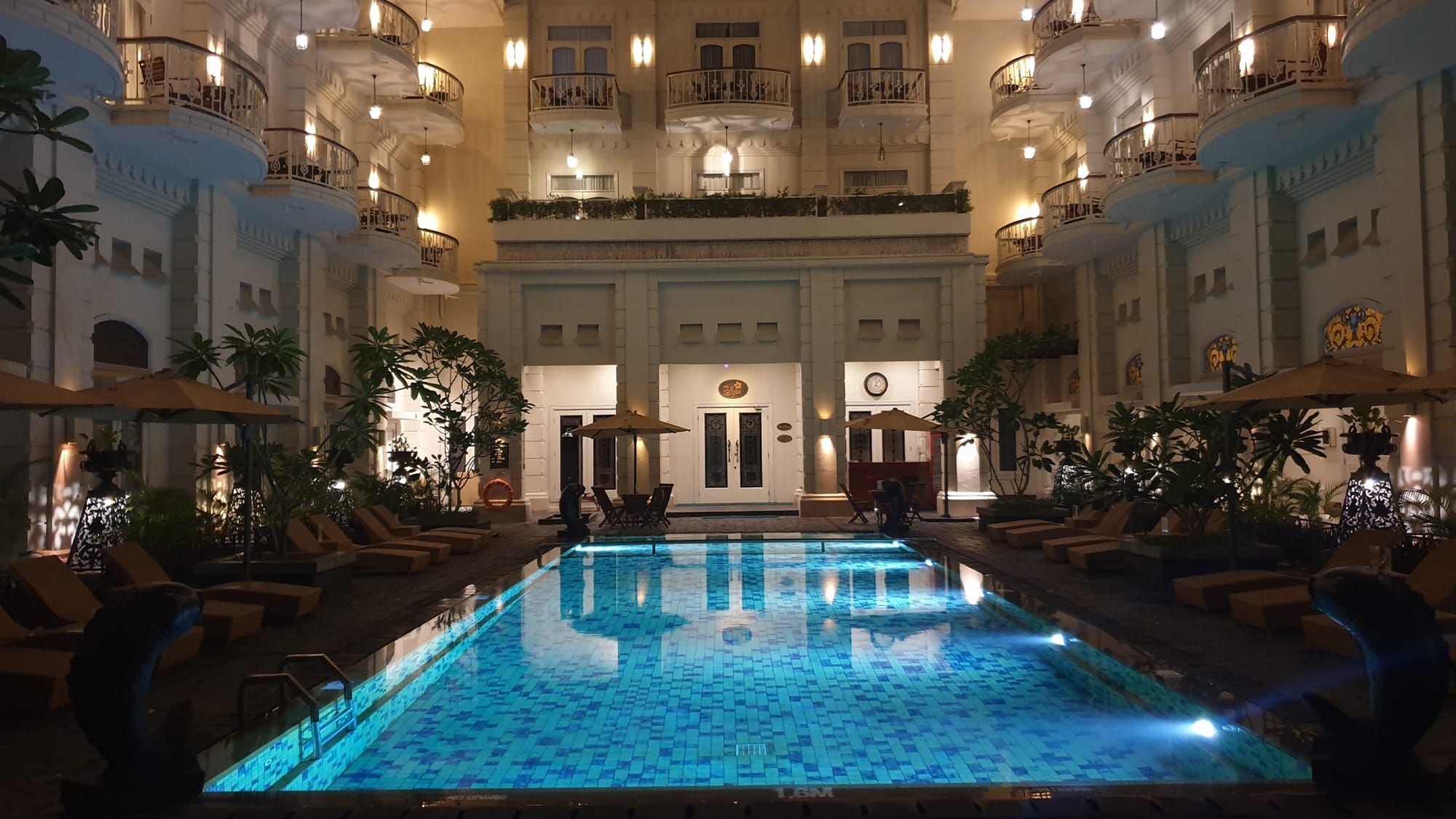 A beautifully illuminated outdoor swimming pool at night, its bright blue water glowing with light
