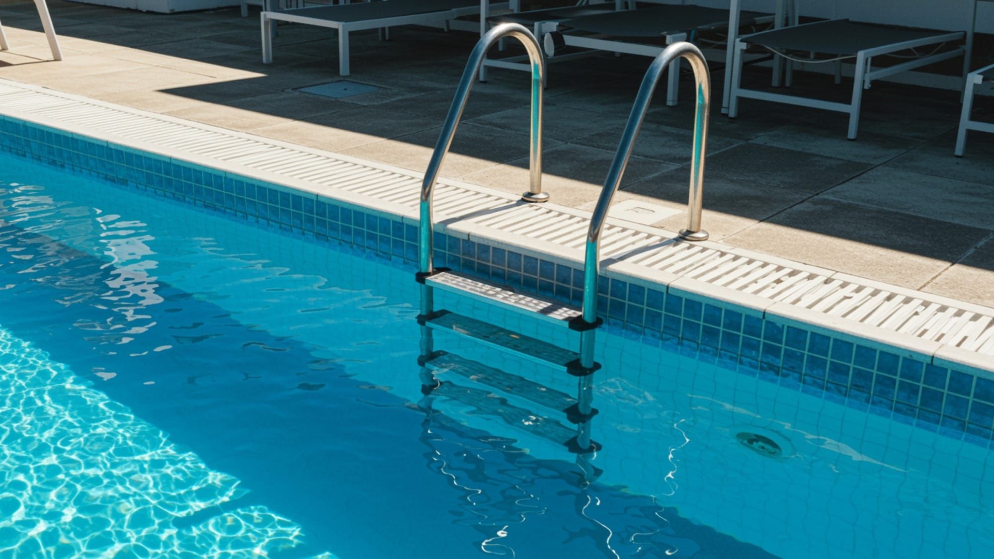 A clean stainless steel pool ladder installed beside a sparkling blue pool, showing the ideal results of regular cleaning and maintenance.
