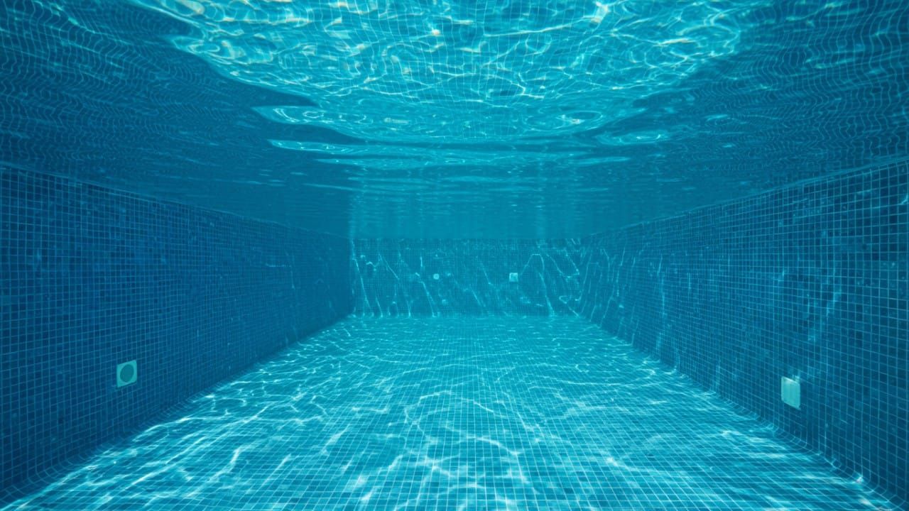 Underwater view of a clear swimming pool with blue mosaic tiles, illustrating clean water and light refraction.