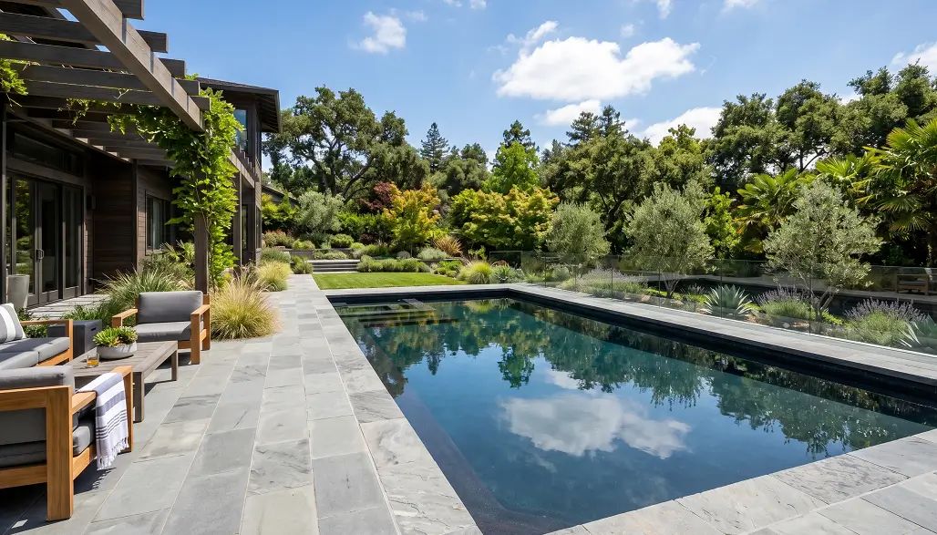 Luxury dark swimming pool reflecting sky in a well-designed garden.
