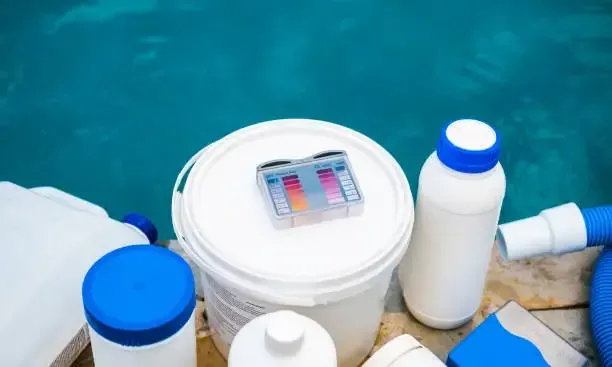 Various swimming pool chemicals and a water testing kit arranged by the poolside.