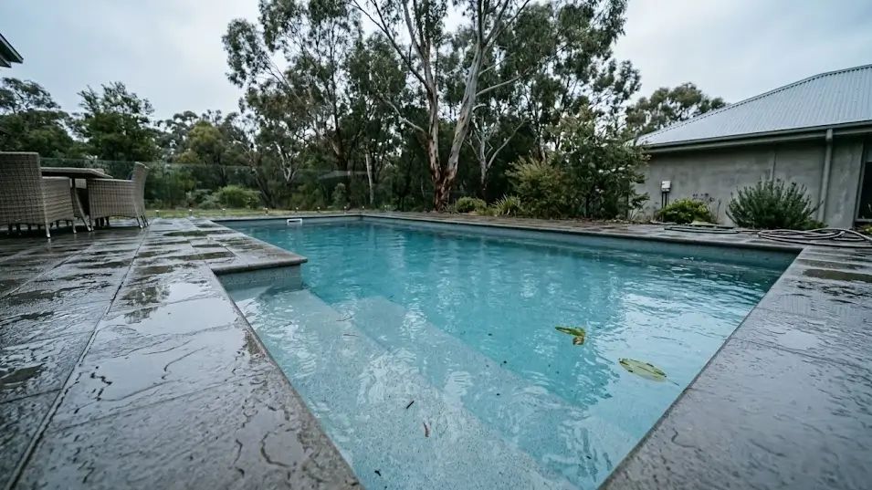 Backyard swimming pool with floating leaves and small worms in the water after heavy rain, showing the common post-storm worm problem.