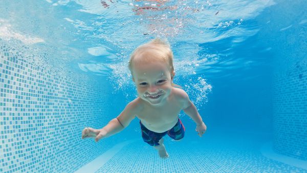 A smiling baby swimming in a pool, demonstrating the joy and confidence of early swimming lessons.