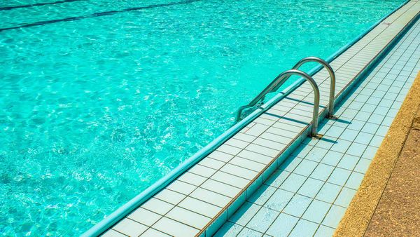 A clear blue swimming pool with a metal ladder, ideal for discussing bromine vs. chlorine sanitizers.