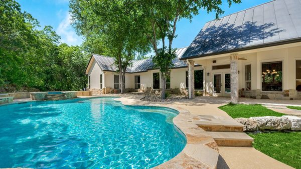 Beautiful home with a sparkling swimming pool surrounded by lush greenery and stone patio.