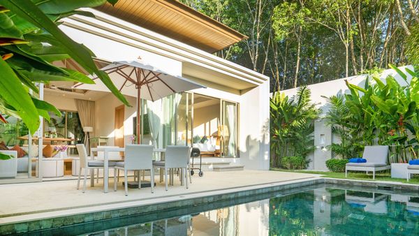 A modern white house with a swimming pool surrounded by lush green tropical plants and trees.