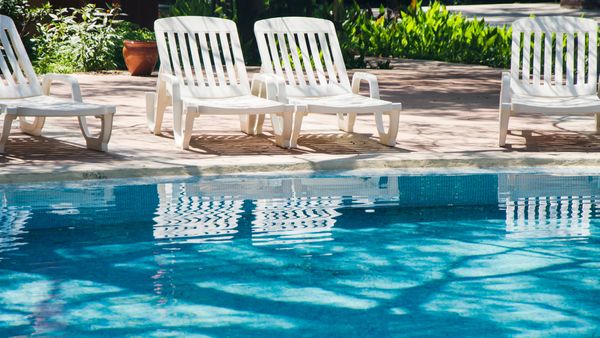 A line of empty white plastic lounge chairs sits beside a sparkling saltwater pool.
