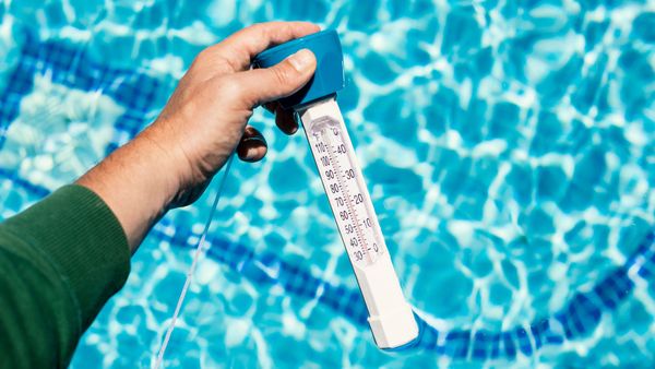A hand holding a thermometer in a swimming pool, illustrating how to measure and maintain the ideal water temperature.