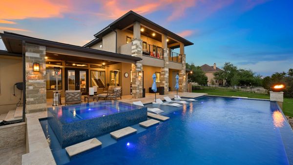 A stunning backyard with a luxurious hotel pool, spa, and patio area under a vibrant sunset sky.