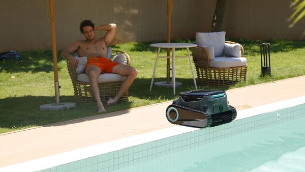 A man relaxes poolside while a robotic pool cleaner navigates the edge of a clean swimming pool.
