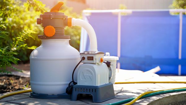 A sand pool filter and pump system are set up on a patio next to an above-ground pool.