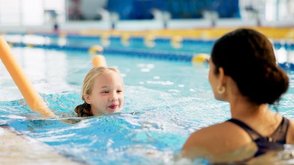 A happy young girl is enjoying her swimming lesson in an indoor pool with her instructor.