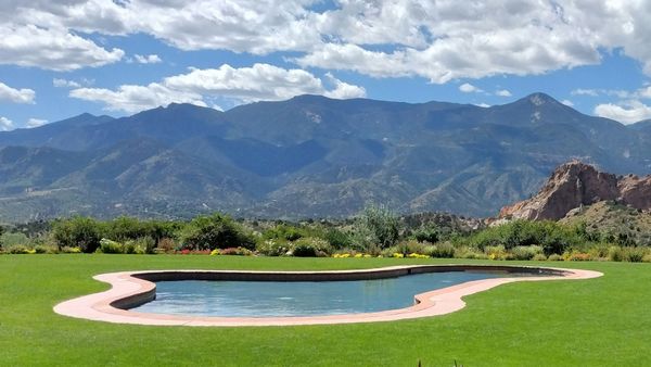 A scenic in-ground swimming pool is surrounded by a green lawn, with mountains in the background.