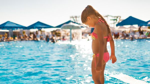 A little girl stood by the pool, testing the water temperature.