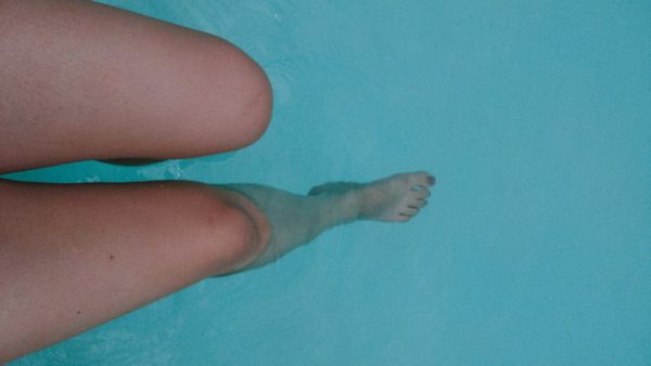 Close-up of a swimmer's legs submerged in clear blue pool water, hinting at prolonged exposure.