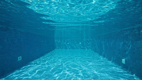 Underwater view of a clear swimming pool with blue mosaic tiles, illustrating clean water and light refraction.