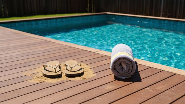 Sandy flip-flops and a towel on the deck next to a clean backyard swimming pool.
