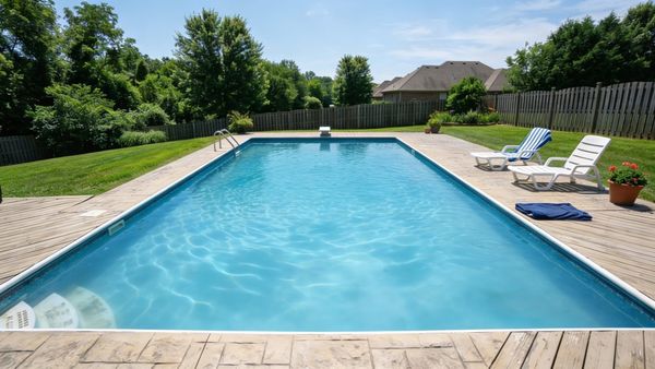 A backyard swimming pool with slightly hazy and dull blue water under bright sunlight.