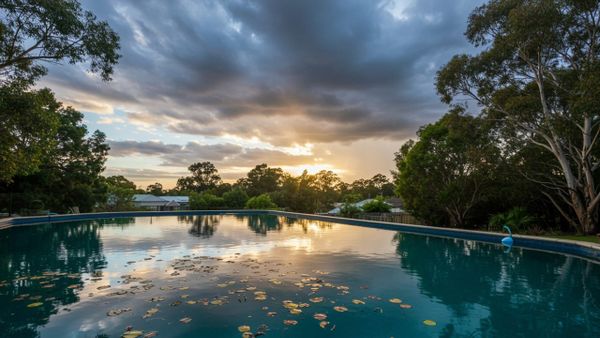 Backyard swimming pool under changing Australian weather with sun, clouds, and floating leaves illustrating weather effects on pool maintenance.
