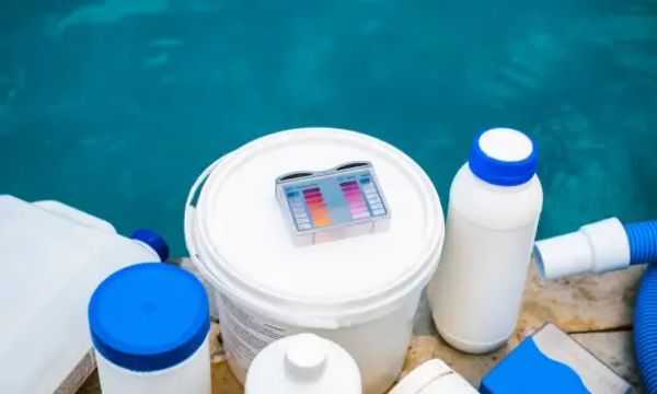 Various swimming pool chemicals and a water testing kit arranged by the poolside.