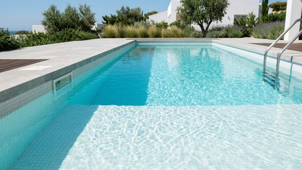 A minimalist, high-end residential swimming pool with perfectly balanced, crystal-clear blue water resting at the ideal skim level.