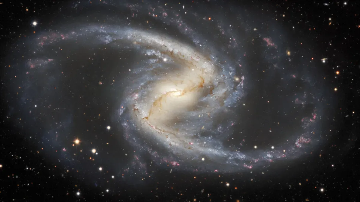 The spiral galaxy has a small and large yellow bar of stars at its center and two large wispy siral arms extending far away