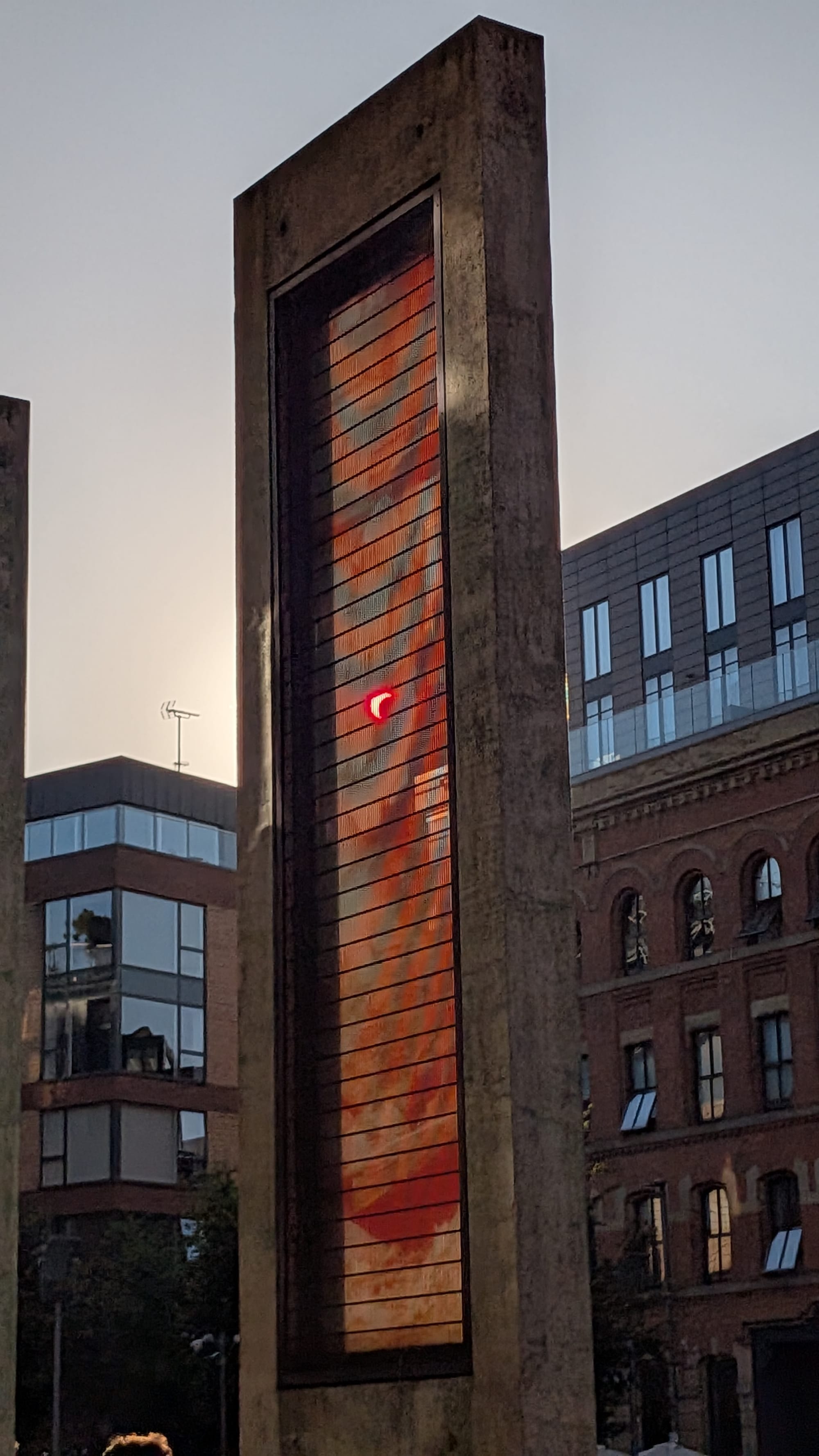 The Sun through the sculpture is visible red and a bit pixelated from this angle. It is mostly covered by the Moon.