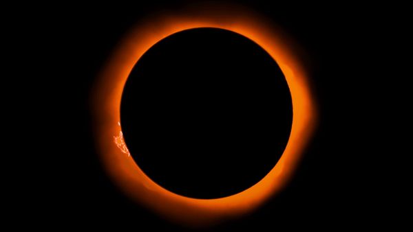 The Sun is completely eclipsed. A large prominense and a bit of the corona are visible beyond the Moon