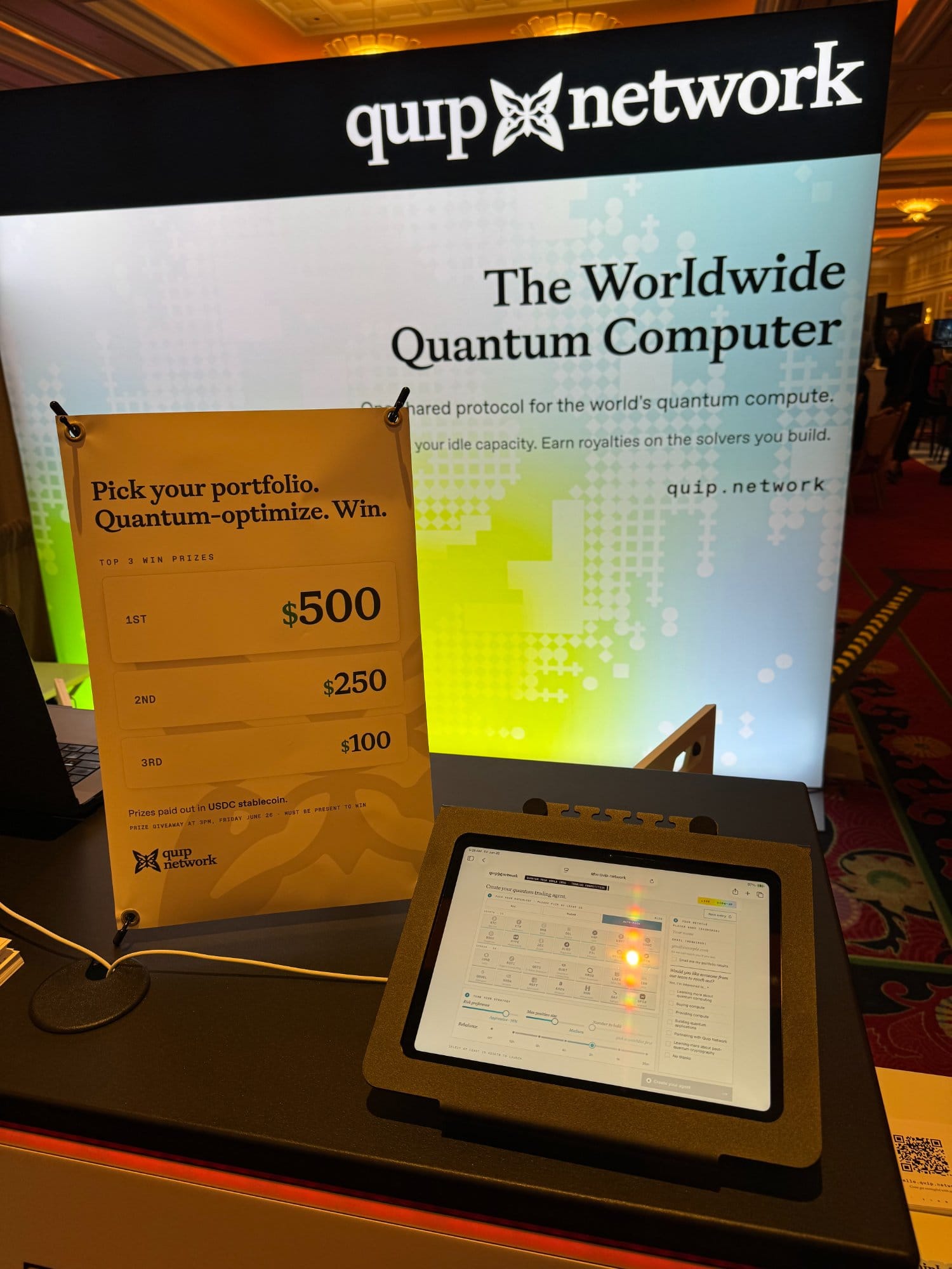 The competition prize sign showing $500, $250, and $100 payouts in USDC beside the trading-agent kiosk.
