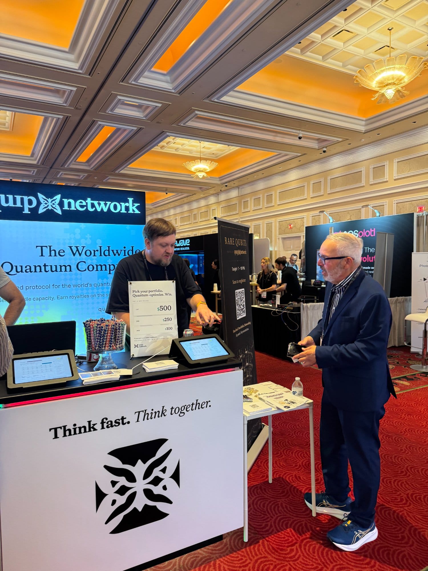 The Quip Network booth on the exhibit floor, with a team member showing the trading competition to an attendee.