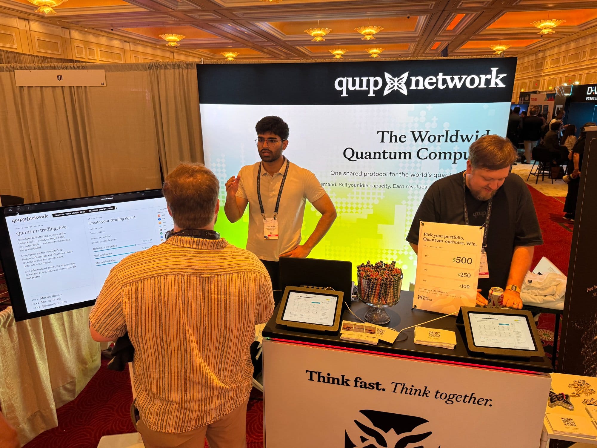 Two Quip Network team members walking a visitor through the trading-agent kiosk at the booth.