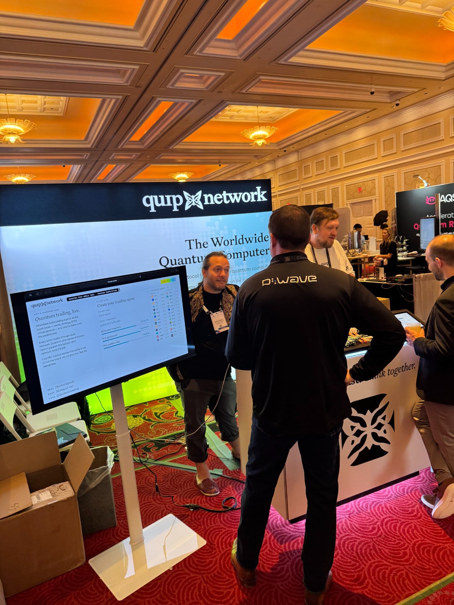 A visitor in a D-Wave shirt at the Quip Network kiosk, with the D-Wave booth beside ours.