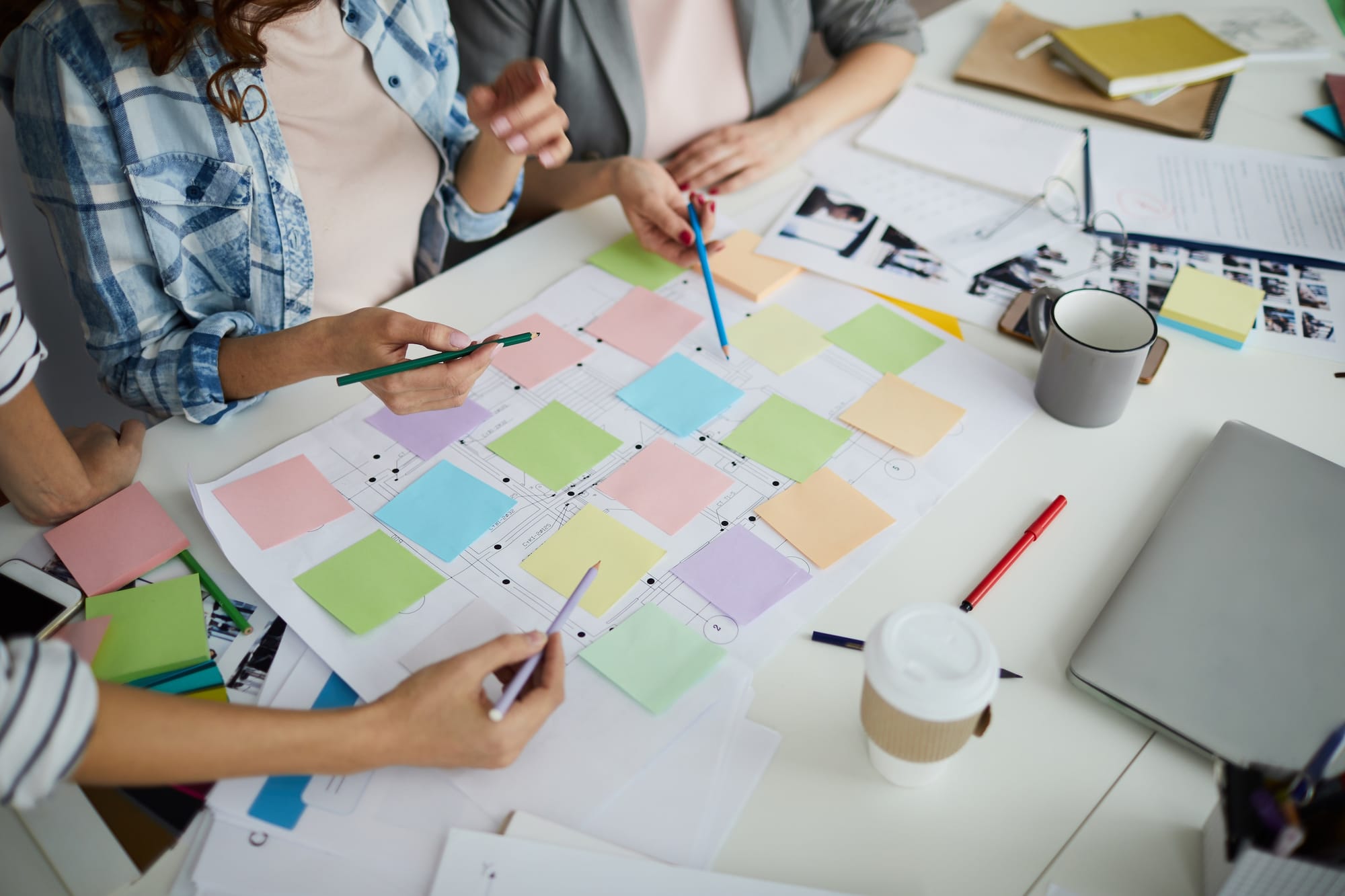 Group of people with pencils and colored post-its set up on a messy desk.