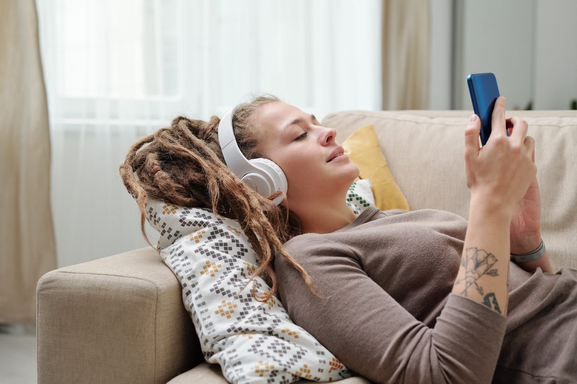 Woman Resting on Sofa With Headphones on looking at smartphone.