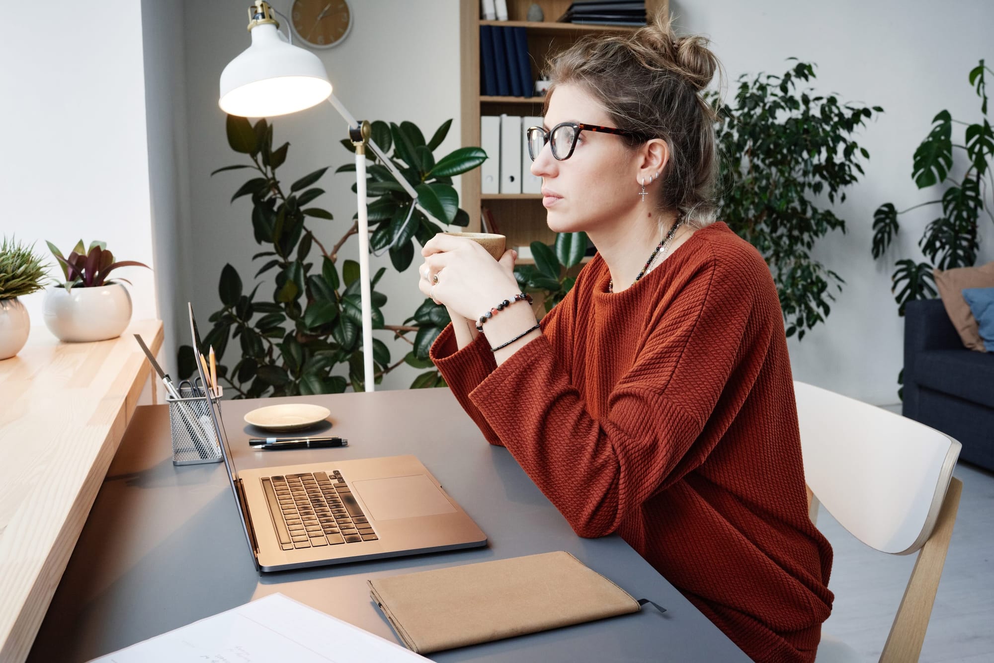 Woman thinking and working on desk with laptop and notebook.