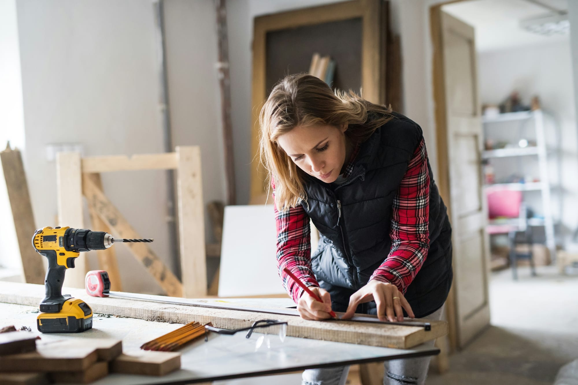 Artisane menuisière qui prend des mesures sur une planche de bois dans son atelier