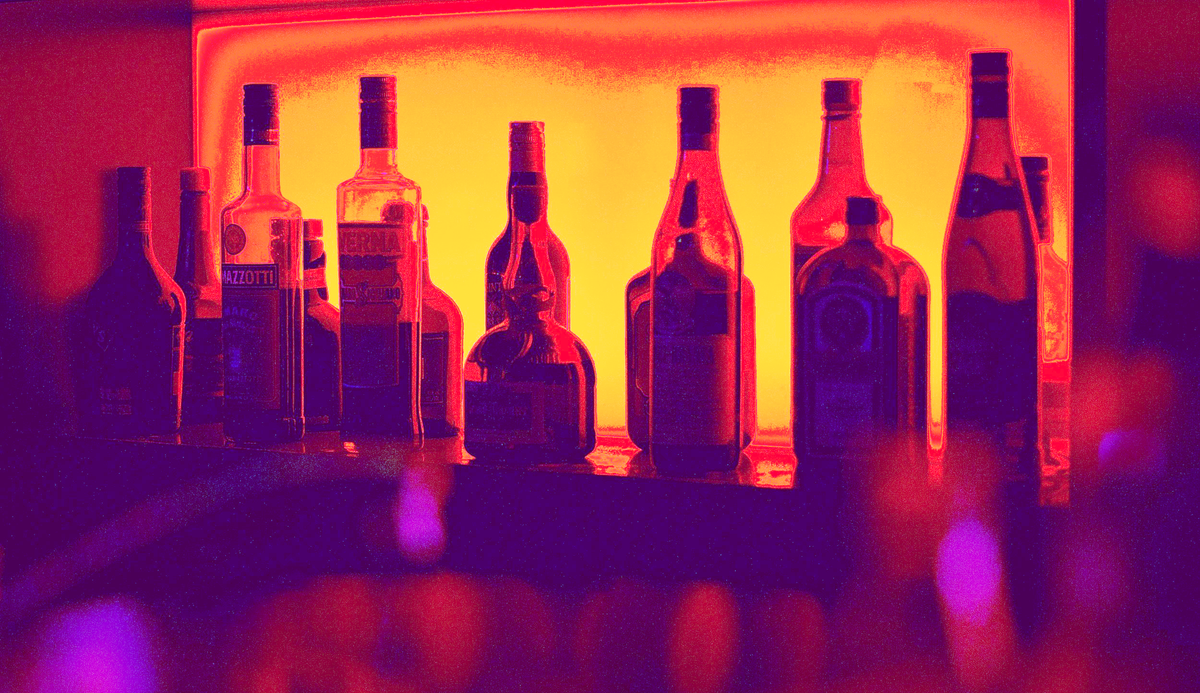 A shelf of liquor in moody pink, orange, and yellow lighting.